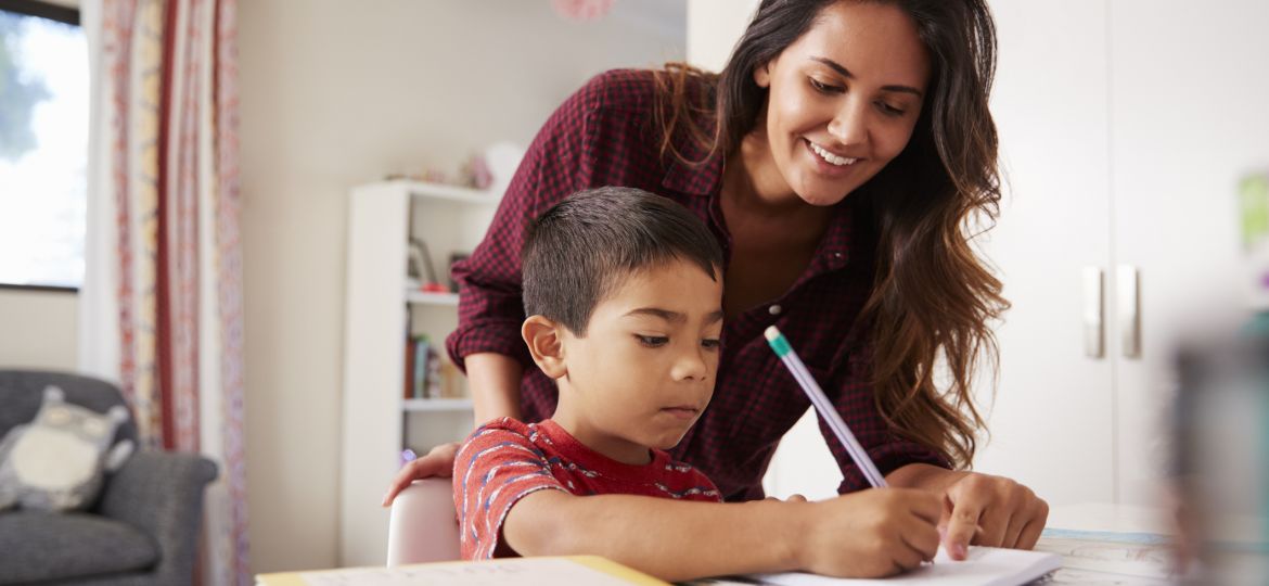 Mother Helping Son With Homework Sitting At Desk In Bedroom