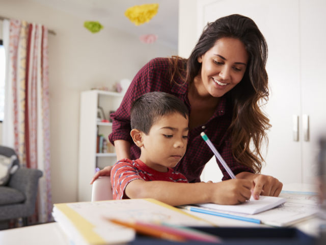 Mother Helping Son With Homework Sitting At Desk In Bedroom